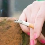 A hand with painted nails holding a lit cigarette